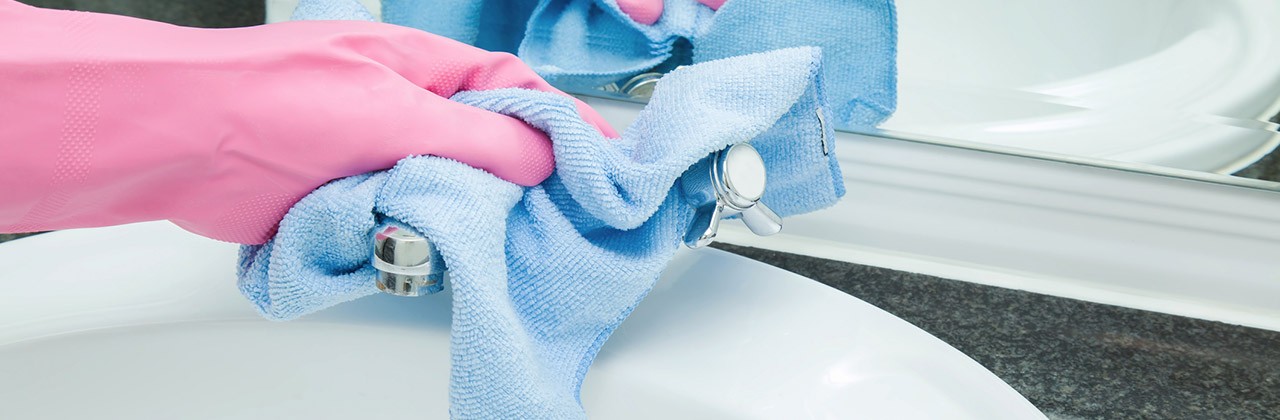 A gloved hand cleans a hotel sink